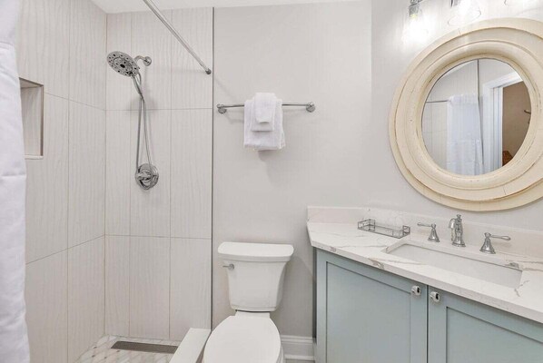 A bathroom with a shower, toilet, sink, and a mirror.