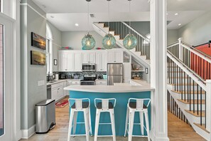 A modern kitchen with white cabinets, a central island, bar stools, and a staircase with a red railing.