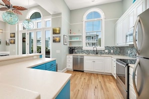 A modern kitchen with white cabinets, a large island, and a view of a house through the window.