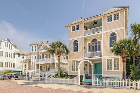 A beachfront hotel with multiple-story buildings, balconies, and a white picket fence.