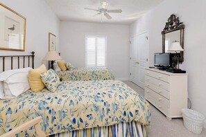 Une chambre à coucher comprenant un lit, une commode, un téléviseur et un ventilateur de plafond.