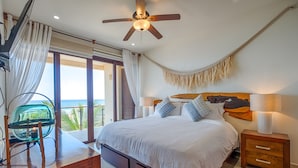 A bedroom with a bed, a desk, a chair, a hammock, and a view of the ocean. - Large upscale penthouse, just right for families or friends, Pool, AC & WiFi! (Akumal)