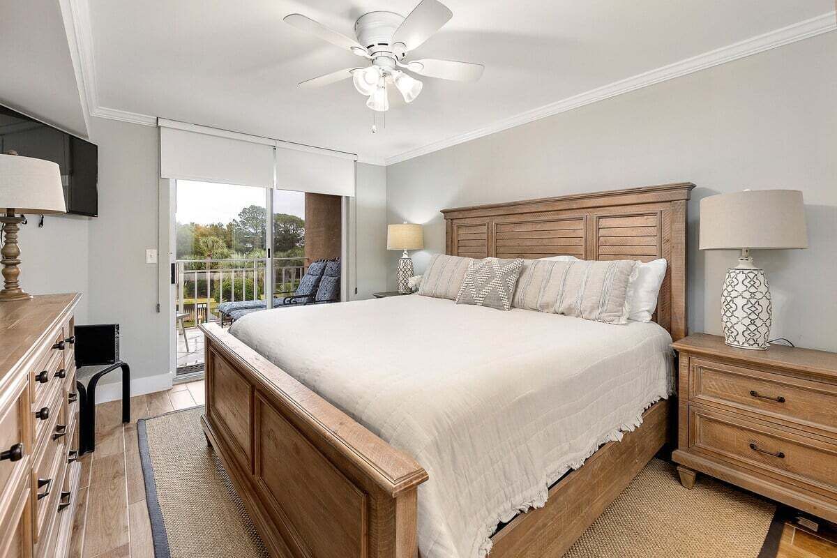 A bedroom with a large bed, wooden headboard, bedside tables, and a ceiling fan.