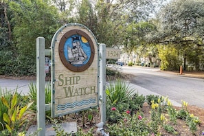 A wooden sign with a ship illustration and the text "SHIP WATCH" in a residential area with houses and greenery. - Oceanfront Condominium (Saint Simons Island)
