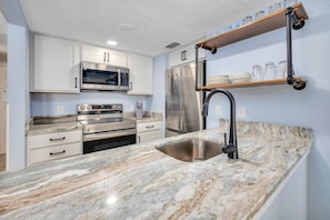 A modern kitchen with white cabinets, stainless steel appliances, a marble countertop, and a built-in sink.