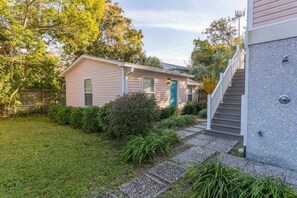 A single-story house with a front porch, a small garden, and a staircase leading to a second level.