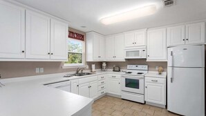 A kitchen with white cabinets, a microwave, a stove, and a refrigerator. - Great Home Close to Beach. (Saint Simons Island)