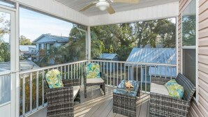 A covered porch with wicker furniture, a ceiling fan, and a view of neighboring houses. - Great Home Close to Beach. (Saint Simons Island)