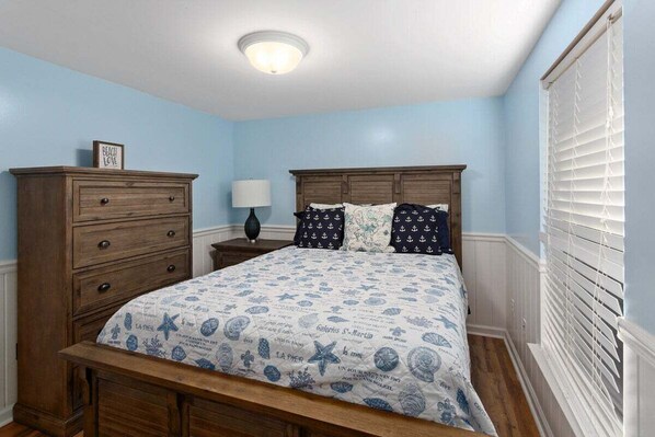 Une chambre à coucher avec un lit en bois, une commode, une table de chevet et une fenêtre avec des stores.