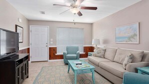 A living room with a ceiling fan, a TV, a sofa, a coffee table, and a patterned rug. - Great Home Close to Beach. (Saint Simons Island)