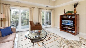 A living room with a glass coffee table, a sofa, a chair, a bookshelf, and a television. - Half a Mile to the Pier and Village! (Saint Simons Island)