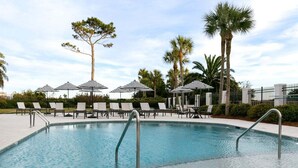 A swimming pool with lounge chairs and umbrellas, surrounded by palm trees and a fence. - Oceanfront Condo with Pool. Ocean View (Saint Simons Island)