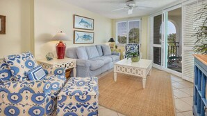 A living room with a sofa, armchair, and coffee table, a ceiling fan, and a view through a glass door to the outside. - Oceanfront Condo with Pool. Ocean View (Saint Simons Island)