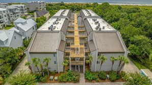 A modern building with a central atrium, surrounded by lush greenery and a view of the ocean. - Oceanfront Condo with Balcony, Pool, Beach Access (Saint Simons Island)