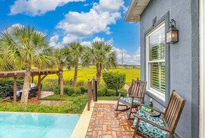 A poolside patio with outdoor furniture, a pergola, and a view of a green field.