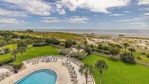 A pool area with lounge chairs and umbrellas, surrounded by greenery and a view of the beach and ocean. - Perfect Beachfront Condo with Direct Ocean View (Saint Simons Island)