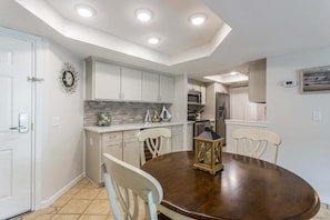 A modern kitchen with white cabinets, a dark wooden dining table, and recessed ceiling lights. - Enjoy Family Fun on St Simons Island! Oceanfront C (Saint Simons Island)