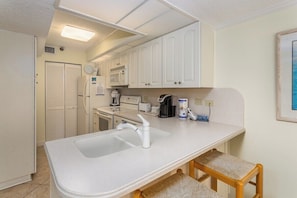 A compact kitchen with white cabinets, a microwave, a coffee maker, and a sink.