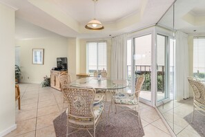 Relax in this stylish living room with a glass-top dining table and wicker chairs, featuring a large sliding glass door leading to a balcony with an outdoor view.