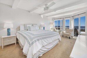 A spacious bedroom with a large bed, a ceiling fan, and a view of the ocean through large windows.
