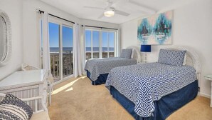 Ein Schlafzimmer mit zwei Betten, einem Deckenventilator, einem Gemälde und Meerblick.