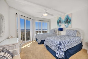 Ein Schlafzimmer mit zwei Betten, einem Deckenventilator, einem Gemälde und Meerblick.