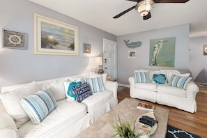 A living room with two white sofas, a coffee table, and a ceiling fan.