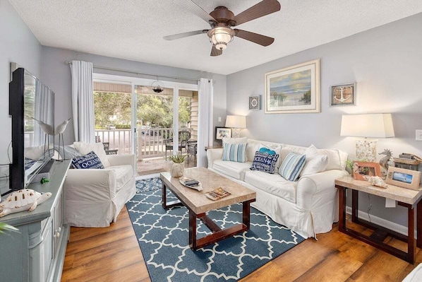 A living room with a ceiling fan, a white sofa, a coffee table, and a view of the outdoors through a sliding glass door.