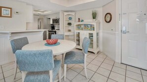 A kitchen with white cabinets, a dining table with blue chairs, and a white door. - Golden Isles Spacious Beachfront Condo (Saint Simons Island)
