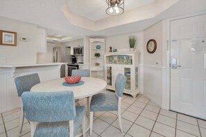 A kitchen with white cabinets, a dining table with blue chairs, and a white door. - Golden Isles Spacious Beachfront Condo (Saint Simons Island)