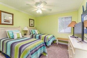 A bedroom with two beds, a ceiling fan, a desk, and a window with blinds. - Ocean Walk Condo L14 (Saint Simons Island)