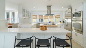 A spacious kitchen with white cabinetry, a central island with bar stools, stainless steel appliances, and a large window providing natural light. - Three Houses Down From Beach In Seaside, FL, Double Lot + 2 Adult Bikes! (Santa Rosa Beach)