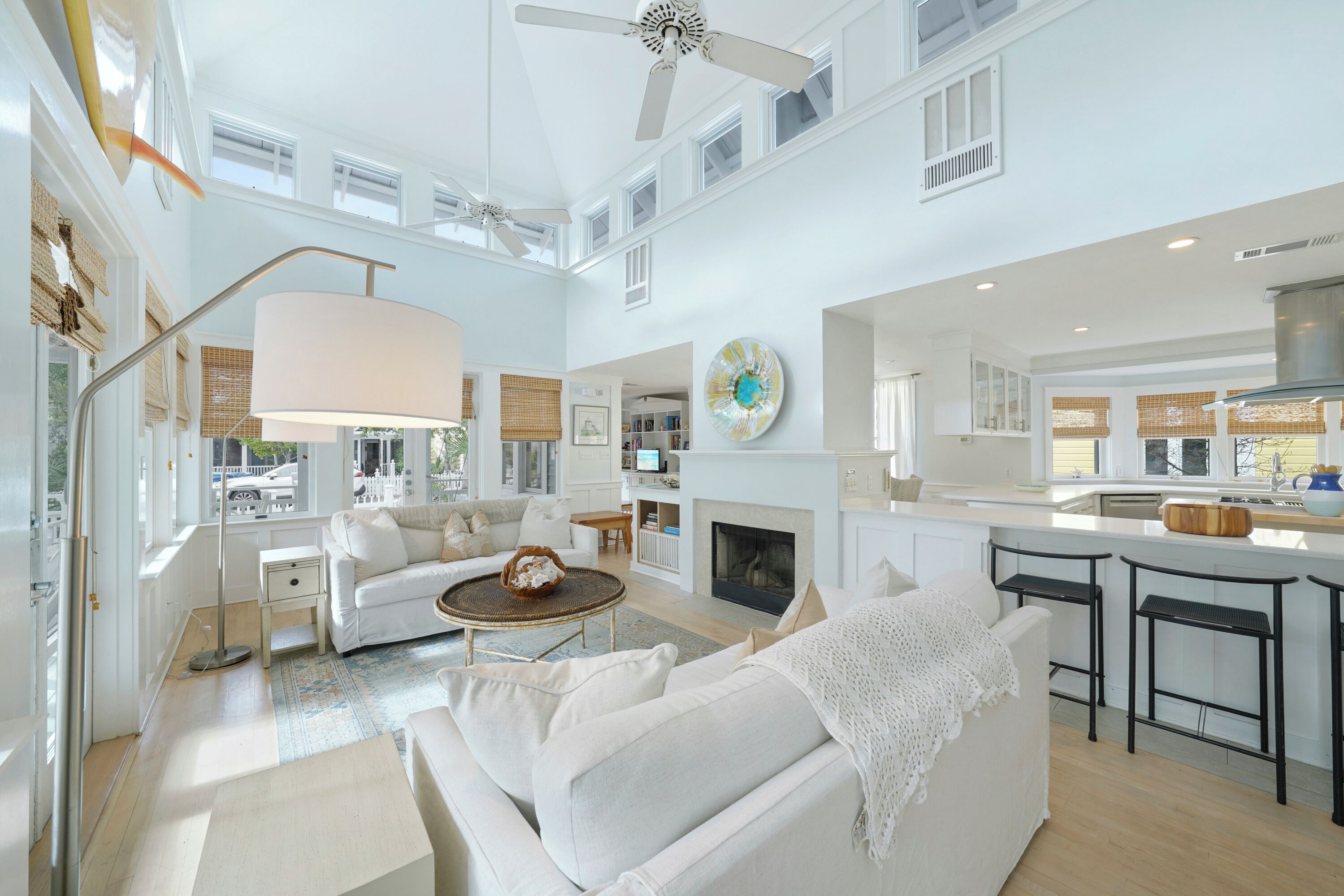 A spacious living area with a fireplace, white sofas, a coffee table, and a kitchen with bar stools.