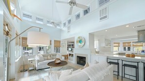 A spacious living area with a fireplace, white sofas, a coffee table, and a kitchen with bar stools. - Three Houses Down From Beach In Seaside, FL, Double Lot + 2 Adult Bikes! (Santa Rosa Beach)