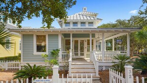 A two-story house with a porch, white picket fence, and a sign indicating the property is for sale. - Three Houses Down From Beach In Seaside, FL, Double Lot + 2 Adult Bikes! (Santa Rosa Beach)