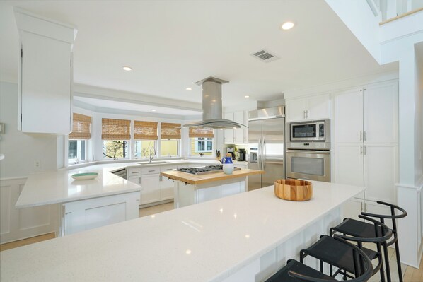 A modern kitchen with white cabinetry, a central island, stainless steel appliances, and a large window. - Three Houses Down From Beach In Seaside, FL, Double Lot + 2 Adult Bikes! (Santa Rosa Beach)