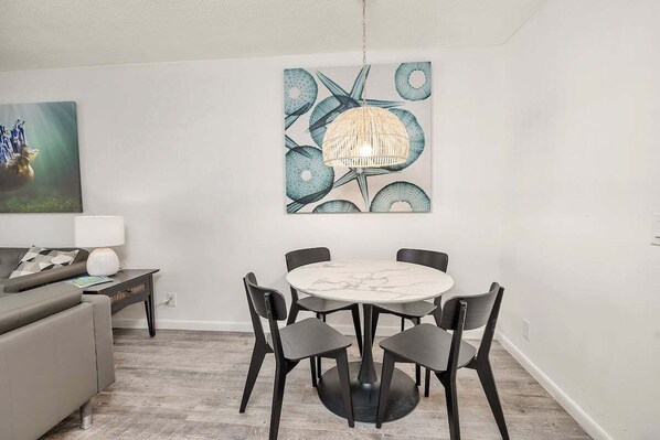 A dining area with a round table and four chairs, a hanging light fixture, and a wall-mounted painting. - Oceanfront Condominium with Great Amenities! (Saint Simons Island)