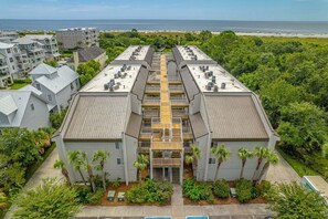 A modern building with a central courtyard, surrounded by lush greenery and a view of the ocean.