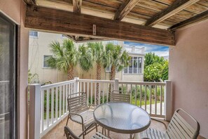 A covered balcony with a round table and chairs, surrounded by a white railing.