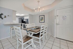A dining area with a wooden table and white chairs, a chandelier, and a white door with a notice on it. - Oceanfront and Great Amenities! (Saint Simons Island)