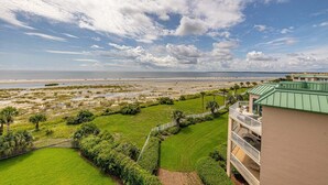 A beachfront property with a green lawn, a white fence, and a building with a green roof. - Beachfront Condo, Room for Multiple Families! (Saint Simons Island)