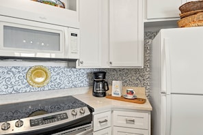 A kitchen with a microwave, stove, coffee maker, and a decorative plate on the counter. - Enjoy a Luxury Getaway at this Oceanfront Condo! (Saint Simons Island)