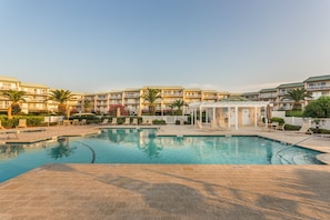 A swimming pool with lounge chairs and a covered area, surrounded by multi-story buildings with balconies. - Enjoy a Luxury Getaway at this Oceanfront Condo! (Saint Simons Island)