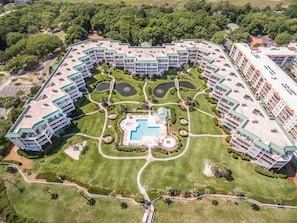Un gran complejo hotelero con varias edificaciones, una piscina central y zonas ajardinadas alrededor.