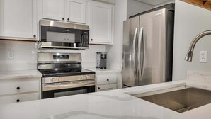 A modern kitchen with white cabinetry, stainless steel appliances including a microwave, oven, and refrigerator, and a marble countertop. - Pet Friendly Oceanfront Condominium (Saint Simons Island)