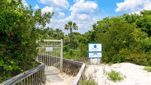 Une entrée fermée par un portail, sur laquelle on peut lire l’enseigne « North Shore Resorts et Hodnett Cooper », le tout entouré d’une végétation luxuriante et d’une plage de sable.