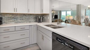 A modern kitchen with white cabinets, a stone backsplash, and a dishwasher. - Oceanfront Condominium with Partial Ocean View! (Saint Simons Island)