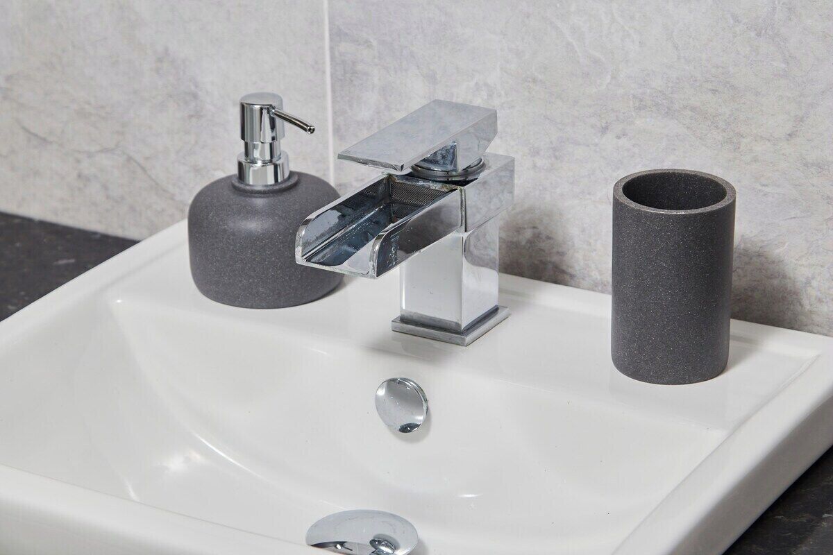 Un lavabo moderno con grifo cromado, dispensador de jabón y un recipiente cilíndrico.