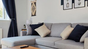 Una sala moderna con un sofá modular gris, una mesa de centro de madera, una lámpara y obras de arte enmarcadas en la pared.