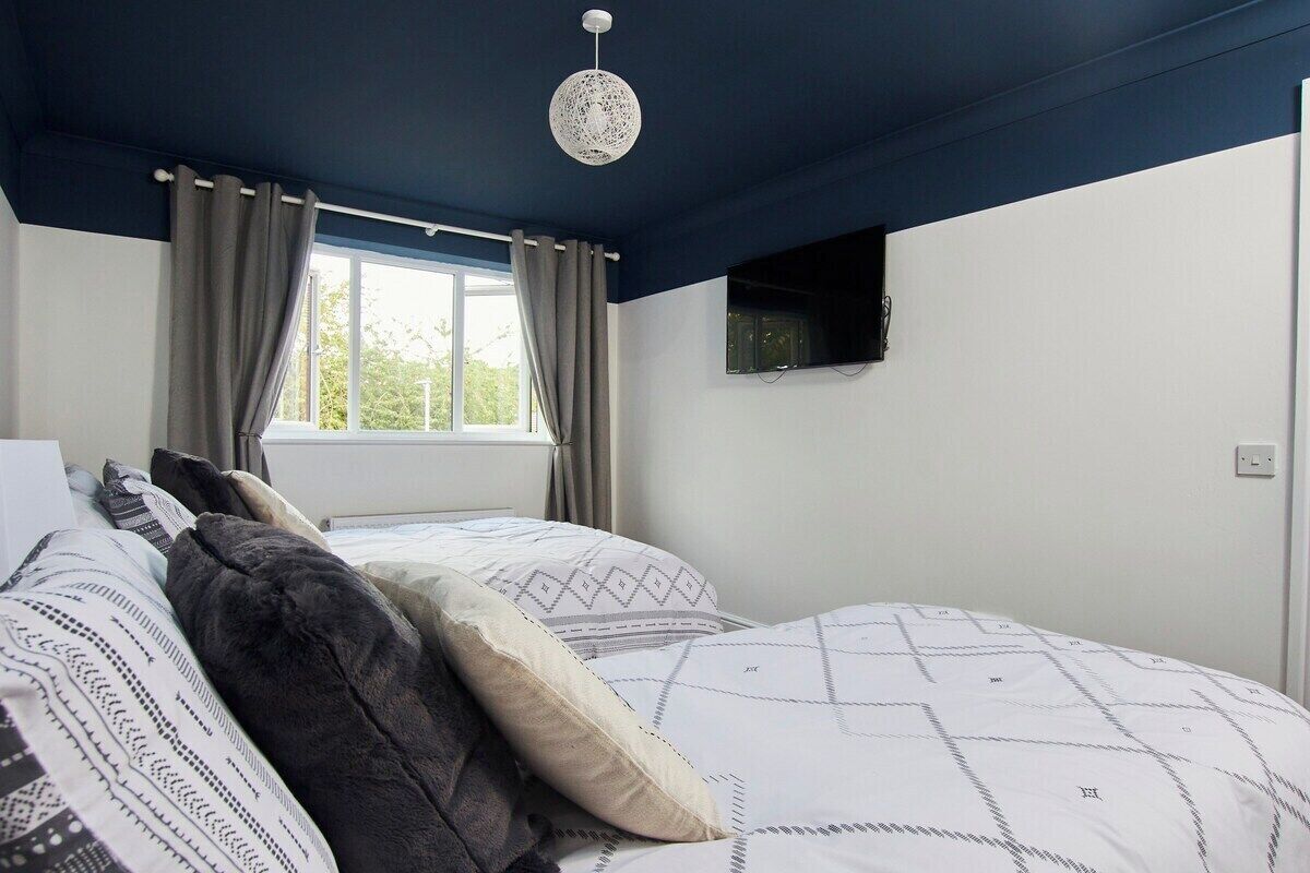 A bedroom with two beds, a window with curtains, a mounted TV, and a hanging light fixture.